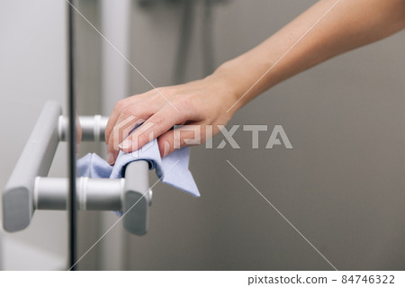 Cleaning glass door handles with an antiseptic wet wipe. Woman hand using towel for cleaning home room door link. Sanitize surfaces prevention in hospital and public spaces against corona virus. 84746322