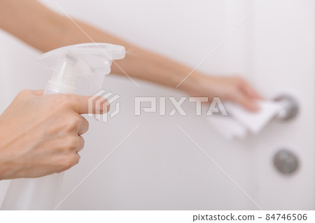 Cleaning white door handles with an antiseptic wet wipe and sanitizer spray. Disinfection in hospital and public spaces against corona virus. Woman hand using towel for cleaning home room door link. 84746506