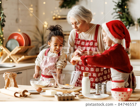 Happy multiracial kids help grandmother to cook Christmas cookies in kitchen during winter holidays Happy multiracial kids help grandmother to cook Christmas cookies in kitchen during winter holidays 84746557