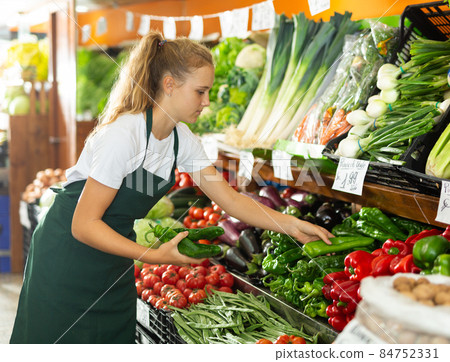 Focused girl who works part-time as a trainee saleswoman puts pepper on showcase 84752331