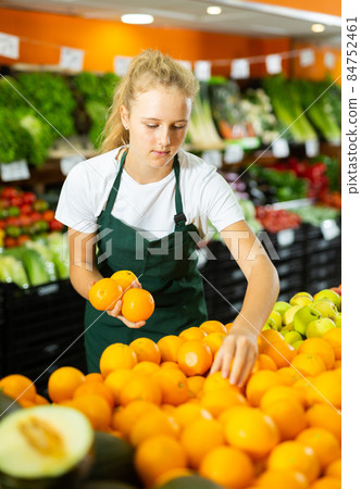 Hardworking girl who works part-time as a trainee saleswoman puts oranges 84752461