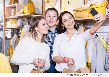 Women friends making selfie in clothes shop, carrying paper bags 84752467
