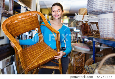 Young customer woman standing with wicker chair in shop for deco 84752477