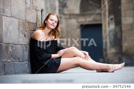 young female sitting barefoot near the stone wall 84752546