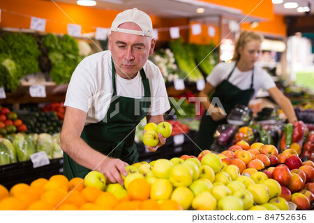 Male seller in uniform holding golden apples 84752636