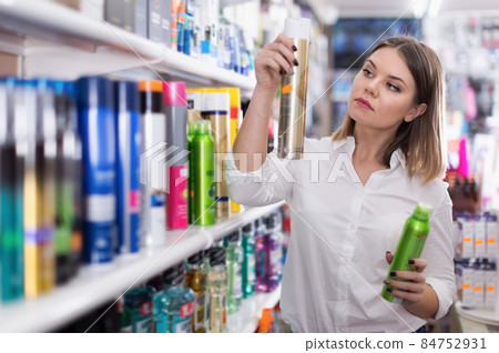 Serious young woman choosing hair care products Serious young woman choosing hair care products 84752931
