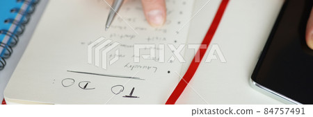 Man holding notepad with to-do list for today near mobile phone closeup 84757491