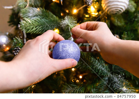 Woman hands decorating Christmas tree with ornaments ball colored in trendy color of year 2022 Very Peri background. Inspired by using color 17-3938, Color of the year concept 84757950