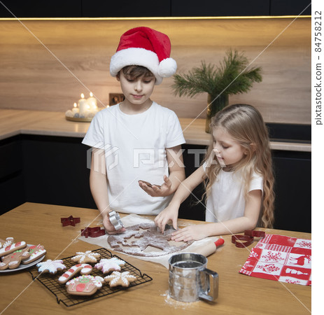 Children - a boy and a girl are preparing gingerbread in the kitchen Children - a boy and a girl are preparing gingerbread in the kitchen 84758212