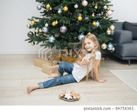 Girl eating Christmas gingerbread near the Christmas tree Girl eating Christmas gingerbread near the Christmas tree 84758361
