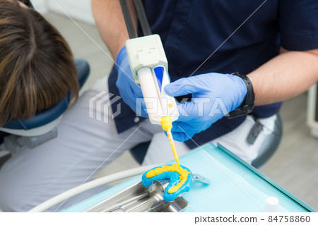 dental impressions, dental prosthetics, a dentist orthopedist holds a model of jaws in his hands and applies polymer from a special syringe dental impressions, dental prosthetics, a dentist orthopedist holds a model of jaws in his hands and applies polymer from a special syringe 84758860