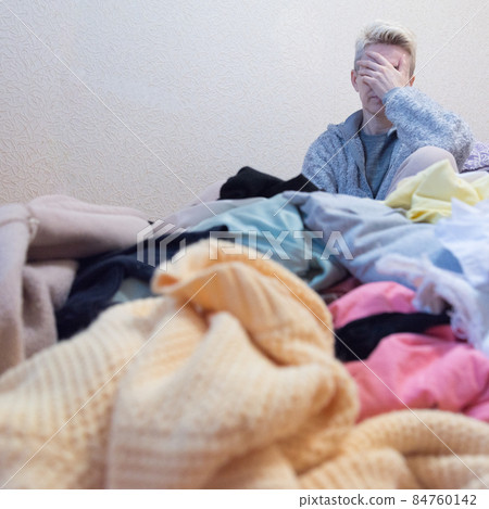 The woman covered her face with her hand. Despair over a lot of clothes. Shopogy concept. Clutter concept. A lot of unnecessary clothes, littering The woman covered her face with her hand. Despair over a lot of clothes. Shopogy concept. Clutter concept. A lot of unnecessary clothes, littering 84760142