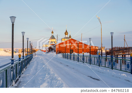 View of a snow-covered bridge and a small Orthodox church in the far North of Russia in the Arctic 84760218