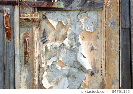 Old shabby wooden door with handle, bolt and latch. Wood surface with peeling white and beige paint texture background. Chunks of paint hang down, corrosion of metal, Rusty metal. Decay and ruins. Old shabby wooden door with handle, bolt and latch. Wood surface with peeling white and beige paint texture background. Chunks of paint hang down, corrosion of metal, Rusty metal. Decay and ruins. 84761335
