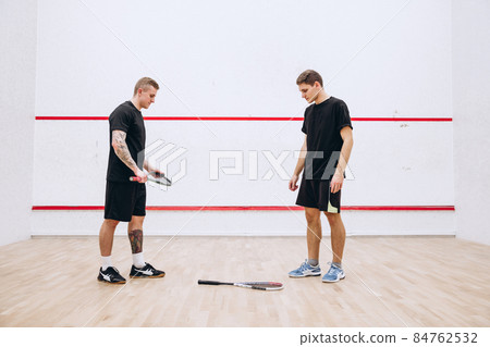 Full-legth portrait of two young sportive men at sport squash studio training, playing team game Full-legth portrait of two young sportive men at sport squash studio training, playing team game 84762532