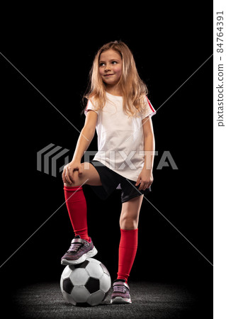 Full-length portrait of girl, child posing with football ball isolated over black background Full-length portrait of girl, child posing with football ball isolated over black background 84764391