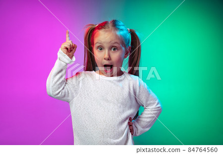 Portrait of little preschool girl, cute kid raising finger up isolated on blue purple studio background in neon light, filter. 84764560