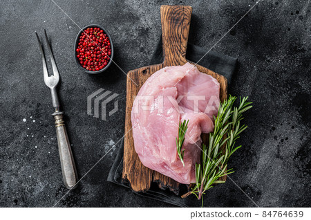 Fresh Raw whole big turkey breast fillet on wooden board. Black background. Top View 84764639