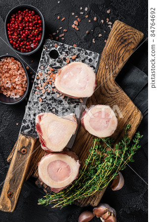 Uncooked Raw veal Marrow bones on butcher board with meat cleaver. Black background. Top view 84764692