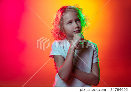 Half-length portrait of little thoughtful boy dreaming isolated on mangenta yellow studio background in neon light, filter. 84764693