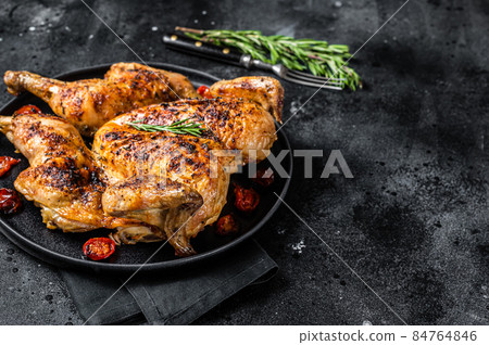 Tobacco whole chicken on plate with herbs and tomato. Black background. Top view. Copy space Tobacco whole chicken on plate with herbs and tomato. Black background. Top view. Copy space 84764846