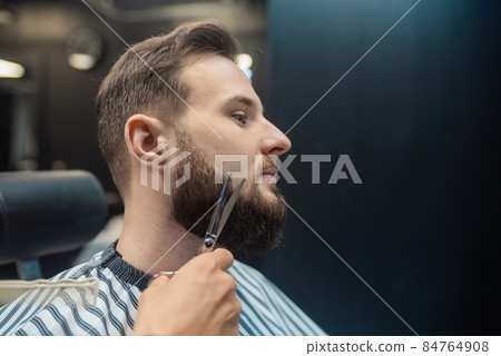 Hairdresser doing haircut of beard using comb and scissors Hairdresser doing haircut of beard using comb and scissors 84764908