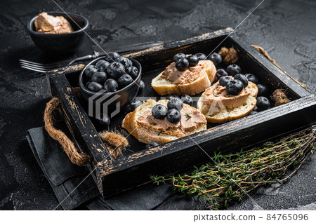 Foie gras toasts, duck liver pate and fresh blueberry in wooden tray. Black background. Top view 84765096
