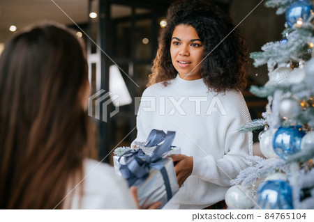 Two young and happy best friends a roommates exchange gifts. Two young and happy best friends a roommates exchange gifts. 84765104