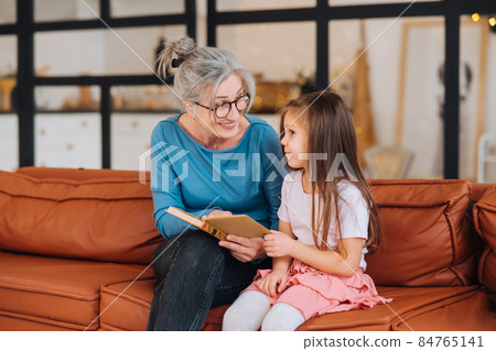 Nice elderly woman grandmother reading story to granddaughter. 84765141