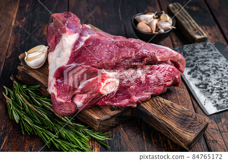 Raw goat thigh on butcher board with meat cleaver. Dark wooden background. Top view. Copy space Raw goat thigh on butcher board with meat cleaver. Dark wooden background. Top view. Copy space 84765172