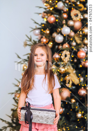 Charming little girl holds a gift on a background of Christmas trees Charming little girl holds a gift on a background of Christmas trees 84765253
