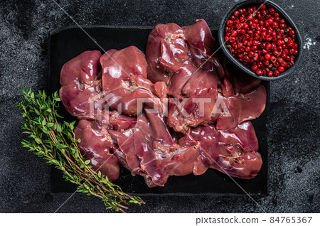 Raw chicken liver meat on marble board with thyme. Black background. Top view 84765367