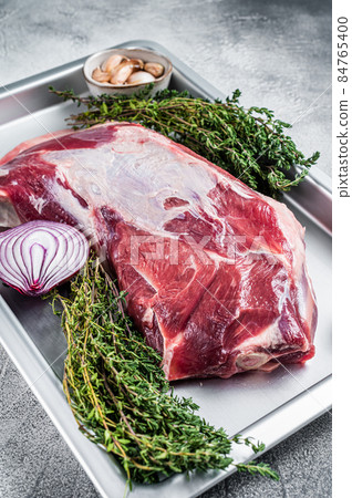 Raw lamb mutton shoulder meat in a baking dish with thyme and garlic. White background. Top view Raw lamb mutton shoulder meat in a baking dish with thyme and garlic. White background. Top view 84765400