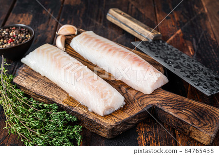 Raw cod loin fillet steak on wooden board with butcher cleaver. Dark wooden background. Top view 84765438