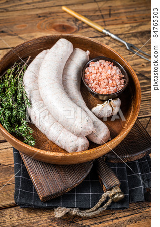 Raw Munich traditional white sausages in a wooden plate with herbs. wooden background. Top view 84765503
