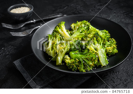 Boiled broccoli with spices in a plate. Black background. Top view 84765718