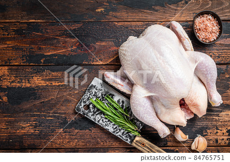 Whole chicken, raw poultry on a butchery table with meat cleaver. Dark Wooden background. Top view. Copy space Whole chicken, raw poultry on a butchery table with meat cleaver. Dark Wooden background. Top view. Copy space 84765751