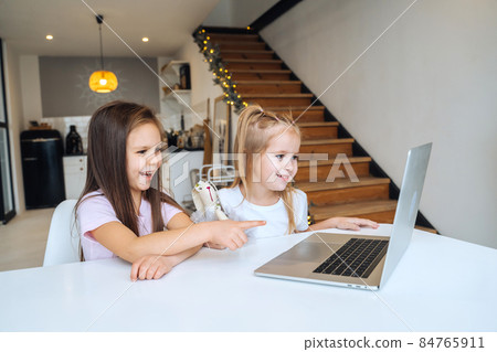 Two little girls playing together at the laptop while sitting at table Two little girls playing together at the laptop while sitting at table 84765911