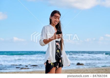 Young woman in headphones with smartphone listening to music on the beach 84766394
