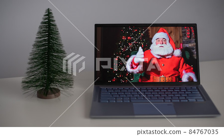 Santa Claus wishes Merry Christmas by video call on a laptop. Remote communication 84767035