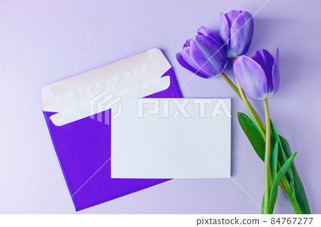 Envelope with invitation to holiday and bouquet of tulips on purple background. Trendy color of the year 2022. Place for text. Envelope with invitation to holiday and bouquet of tulips on purple background. Trendy color of the year 2022. Place for text. 84767277
