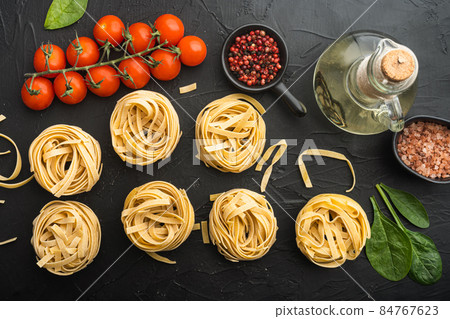 Rolled tagliatelle shape of italian pasta with ingredients, on black stone background, top view flat lay Rolled tagliatelle shape of italian pasta with ingredients, on black stone background, top view flat lay 84767623