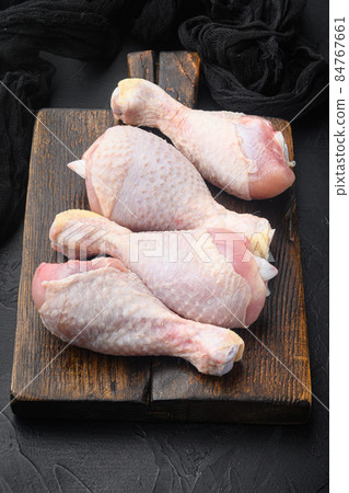 Primal cut of raw chicken legs, with chicken thighs and drumsticks, on wooden cutting board, on black stone background 84767661