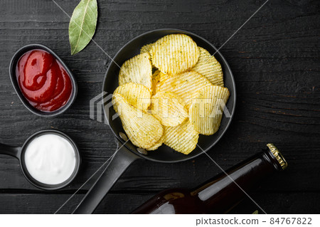 Crispy potato chips. Slices of potato, roasted with sea salt , and bottle of beer , on black wooden background, top view flat lay Crispy potato chips. Slices of potato, roasted with sea salt , and bottle of beer , on black wooden background, top view flat lay 84767822