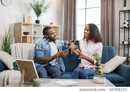 African american couple sitting on couch and chatting African american couple sitting on couch and chatting 84768233