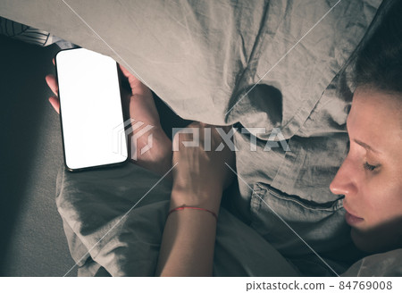 A woman falls asleep in bed with a smartphone in her hand. A woman falls asleep in bed with a smartphone in her hand. 84769008