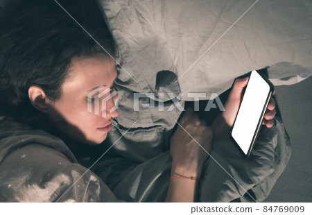 A woman falls asleep in bed with a smartphone in her hand. A woman falls asleep in bed with a smartphone in her hand. 84769009