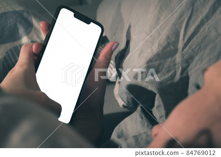 A woman lies in bed and uses a smartphone. 84769012