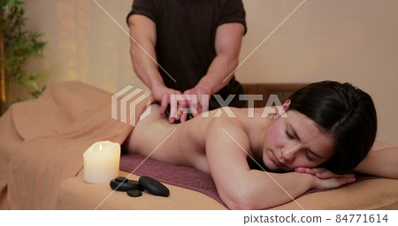 Woman relaxing at spa center with a lastone therapy. Girl with eyes closed lying on massage table at spa salon. 84771614