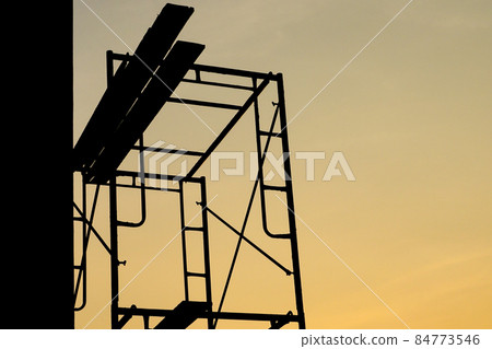Silhouette of steel scaffolding with wooden plate at the construction site isolated on sunset sky. Day off 84773546